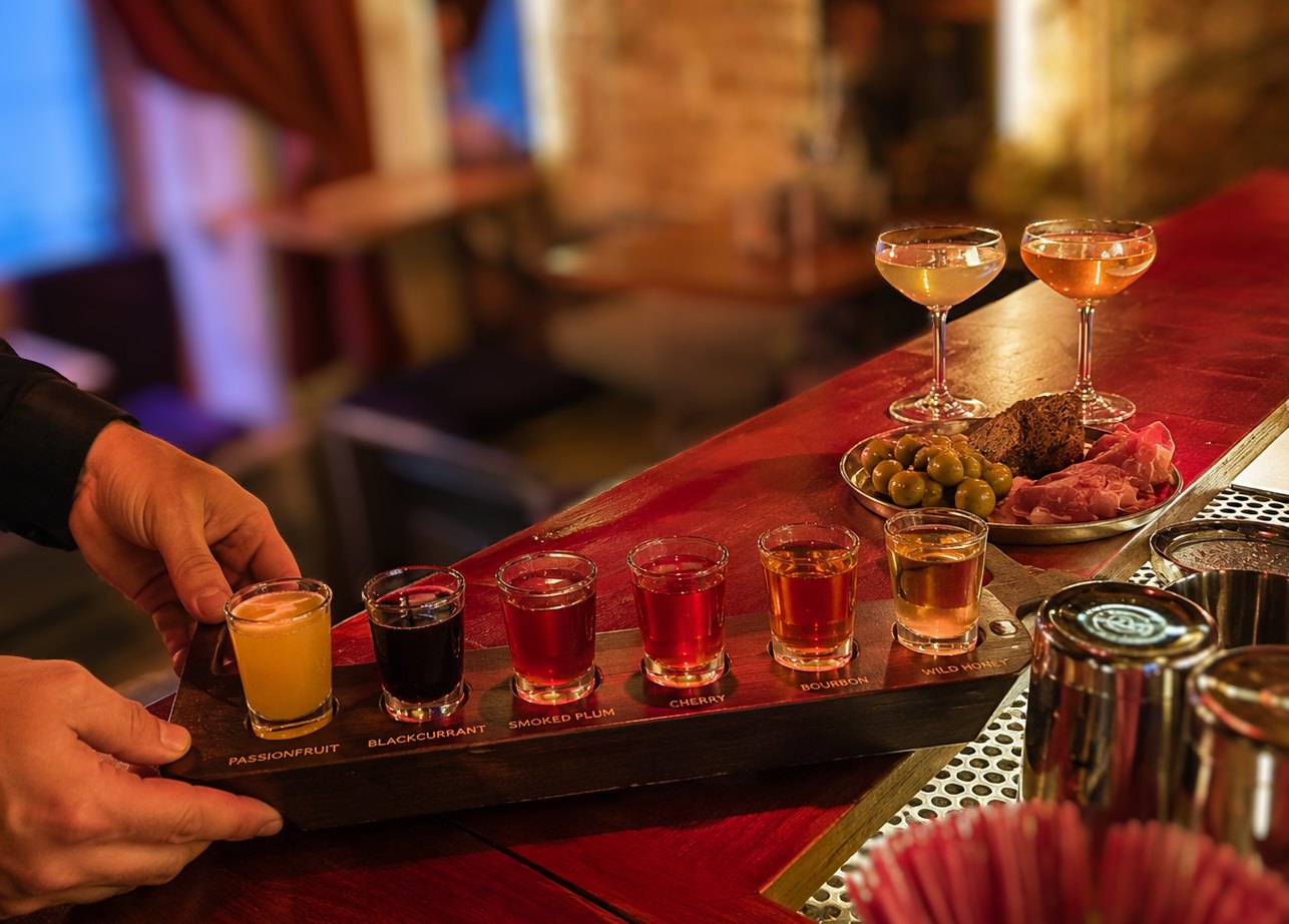 A wooden tasting flight of house infusions with one-sip coupes and bites
