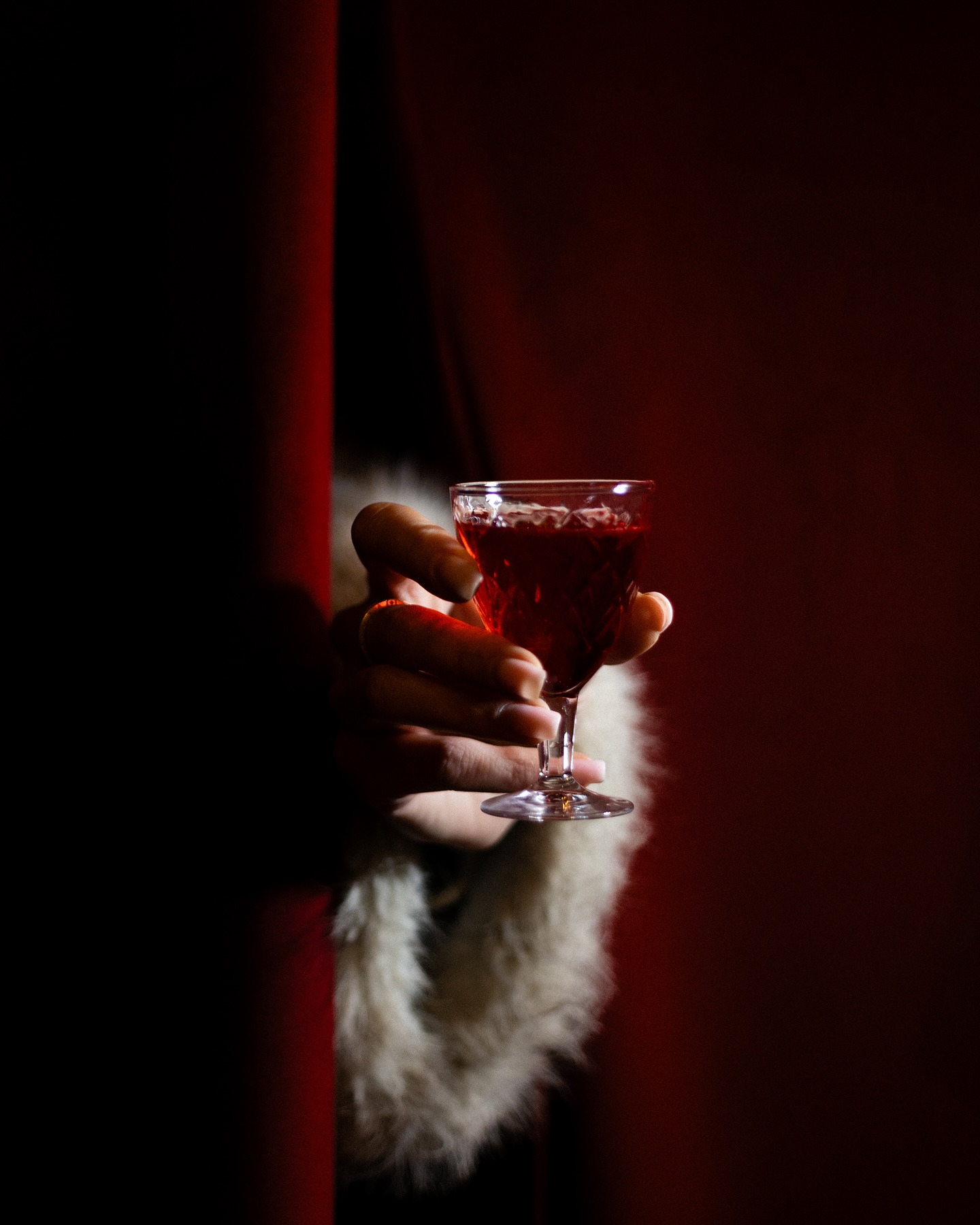 A jewel-red cocktail offered from behind velvet drapery
